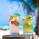 Two cocktails with umbrellas on a wooden surface with a beach background