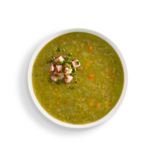 Green soup with ham and vegetables in a white bowl on a white background
