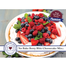 No Bake Berry Blitz Cheesecake Mix packaging and prepared dessert presentation. A white plate holds a cheesecake topped with mixed berries, strawberries, blueberries, raspberries, mint leaves, and graham cracker crumbs.