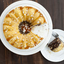 Bundt cake with a slice taken out on a white plate, served on a wooden table.