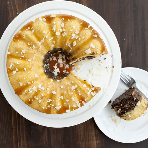 Bundt cake with a slice taken out on a white plate, served on a wooden table.
