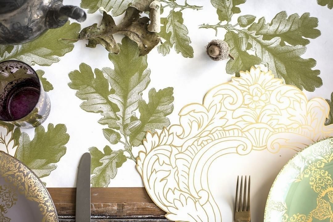 Decorative table setting with green oak leaf patterned paper, gold-rimmed plates, and cutlery.