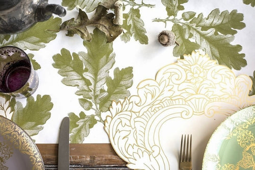 Decorative table setting with green oak leaf patterned paper, gold-rimmed plates, and cutlery.