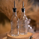 Two glass bottles with pourer stoppers on a wooden stump with a blurred tan background.