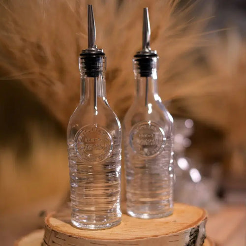 Two glass bottles with pourer stoppers on a wooden stump with a blurred tan background.