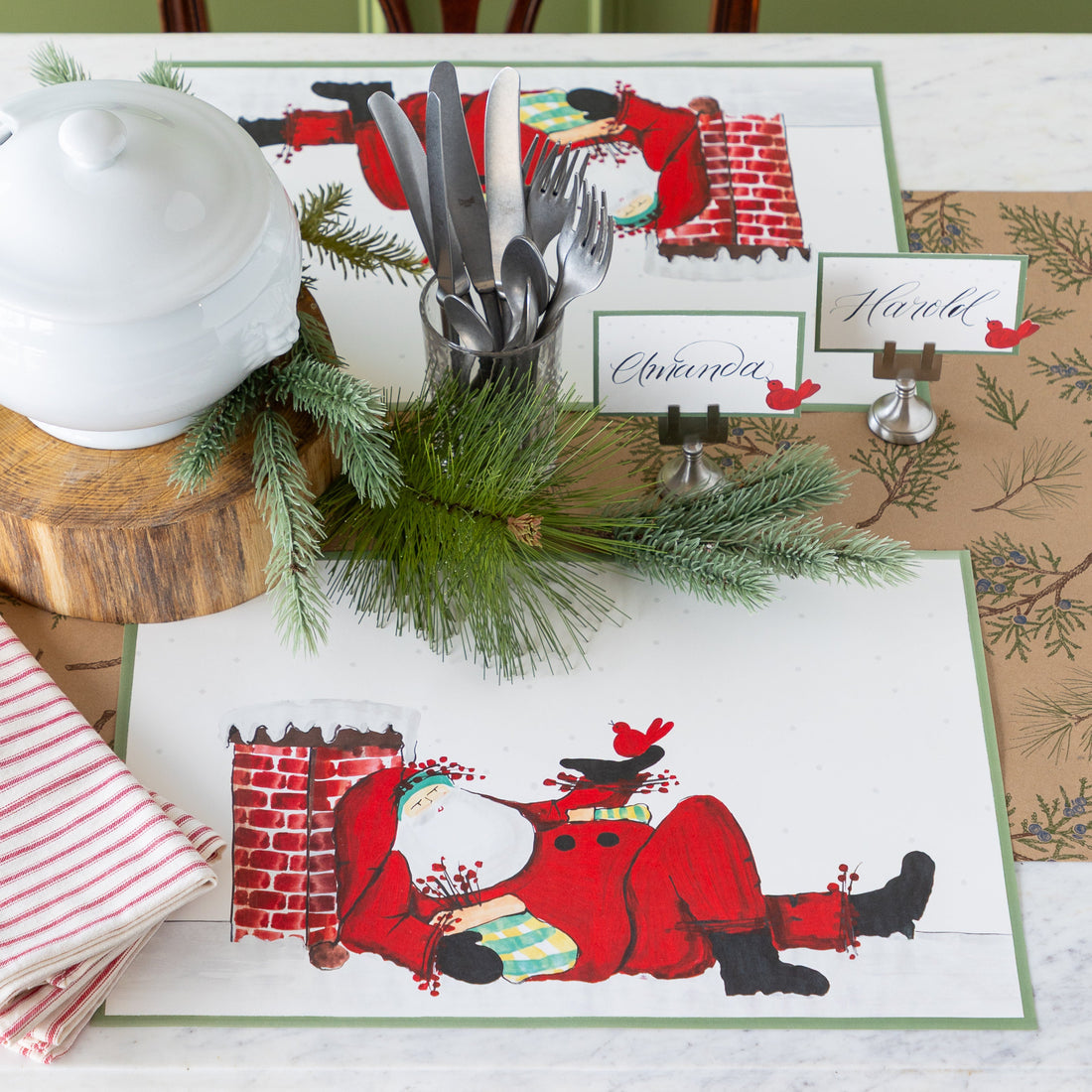 Christmas-themed table setting with Santa Claus design on placemats, silverware, and name cards.