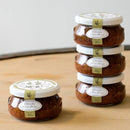Three jars of olive pesto stacked on a wooden surface with a white background