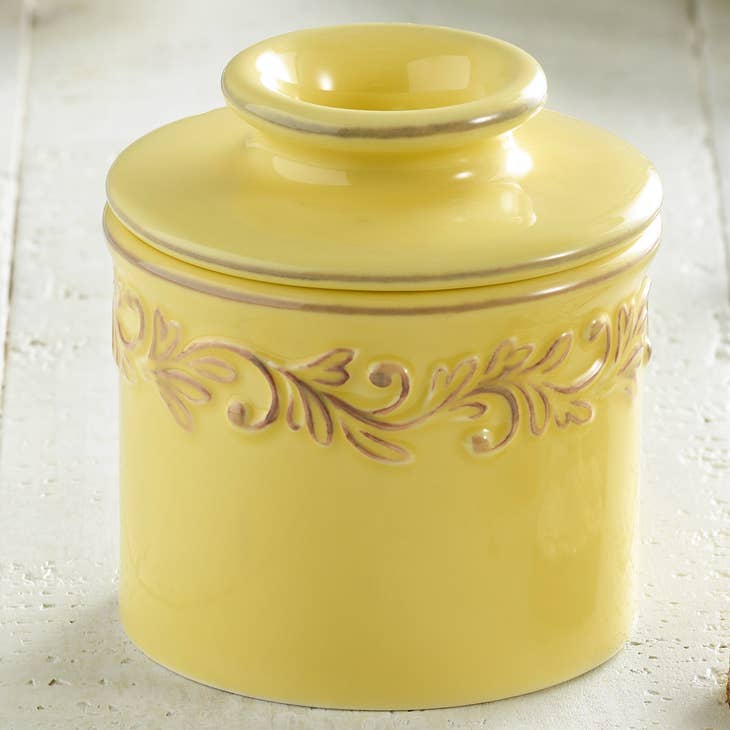 A yellow ceramic Butter Bell crock with intricate leaf embossing.