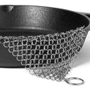 Metal chainmail scrubber over a cast iron skillet on a white background