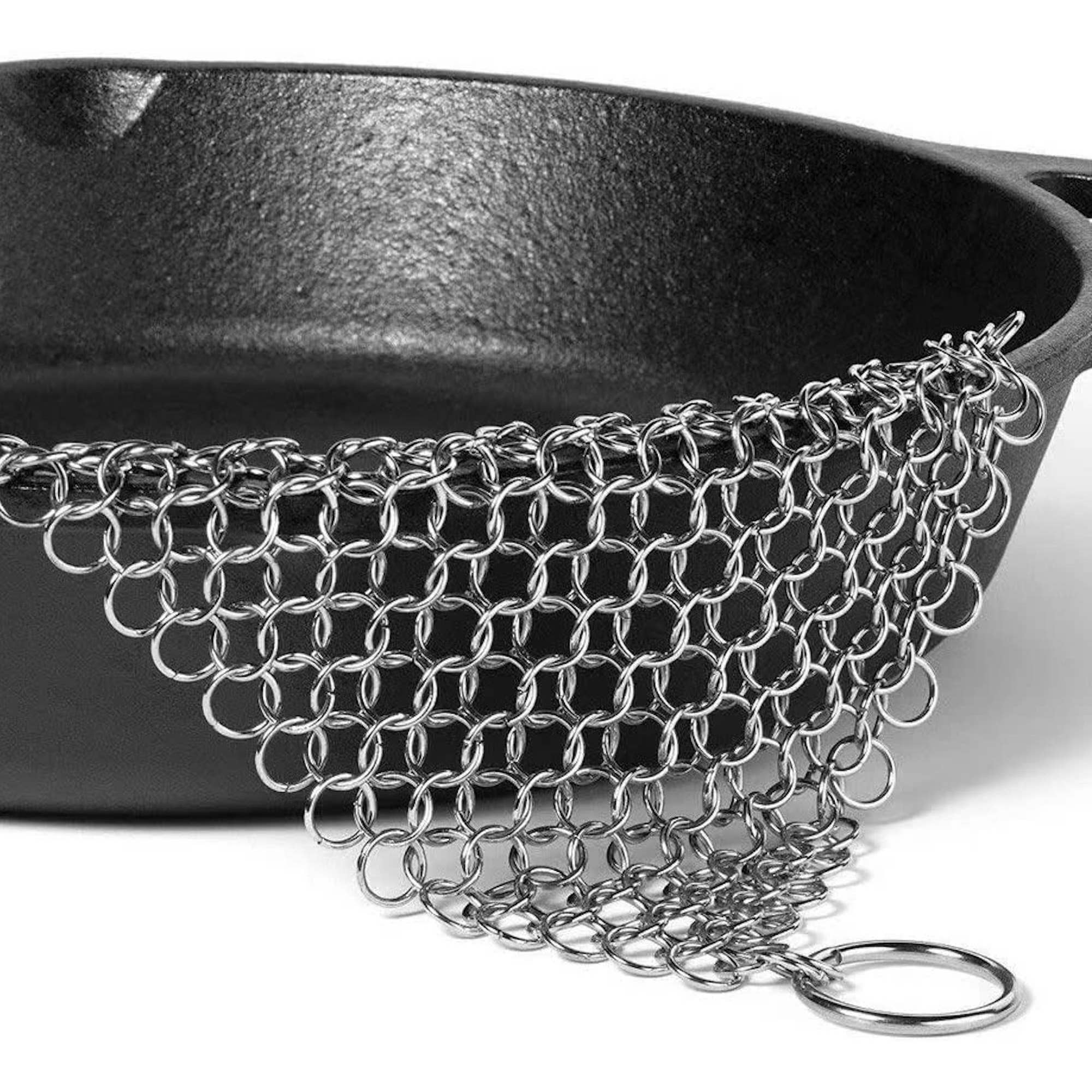 Metal chainmail scrubber over a cast iron skillet on a white background