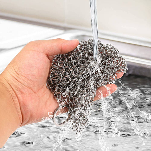 Hand holding a metal scrubber under running water in a sink