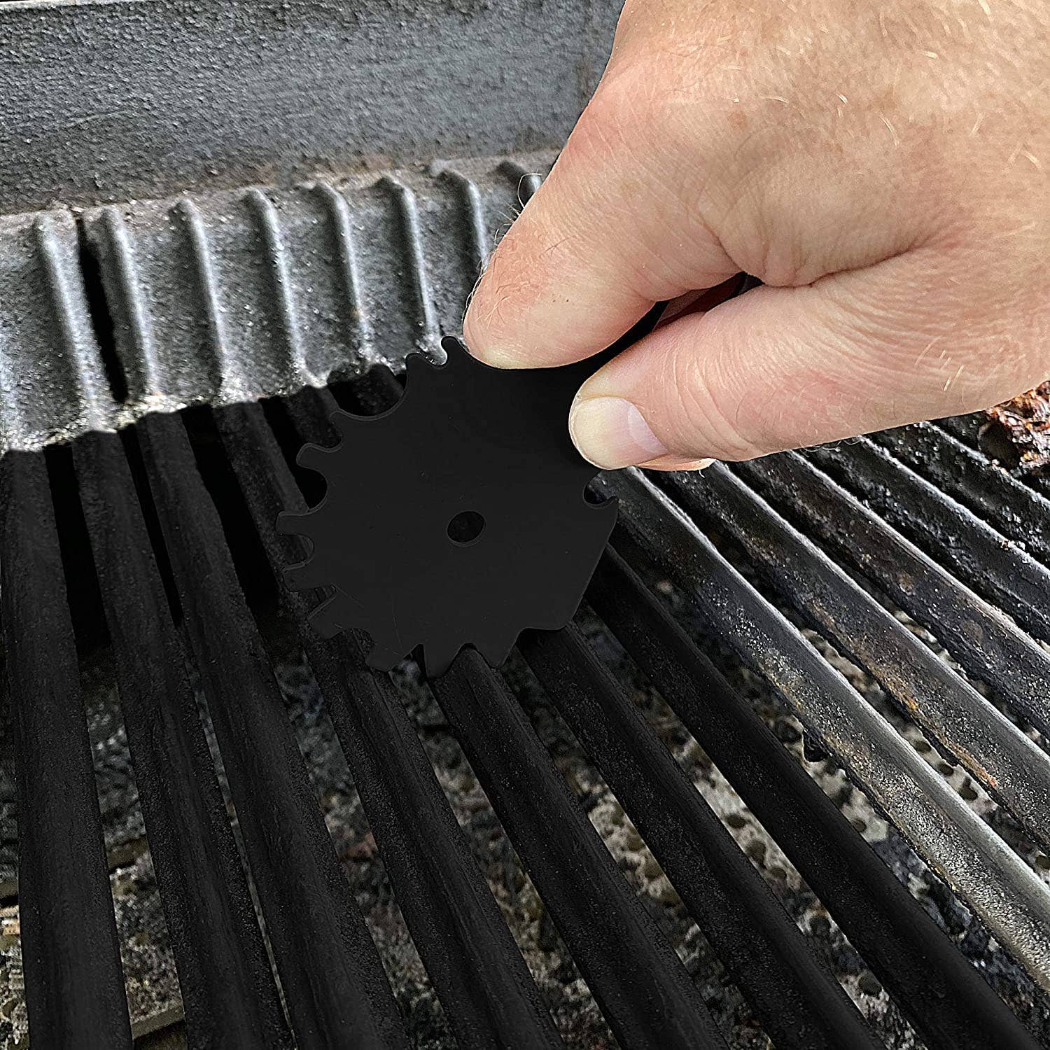 Person using a black grill brush on a grill grate