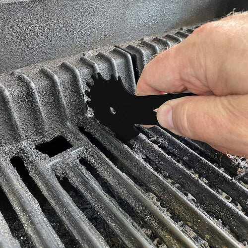 Person using a black tool to clean a grill grate