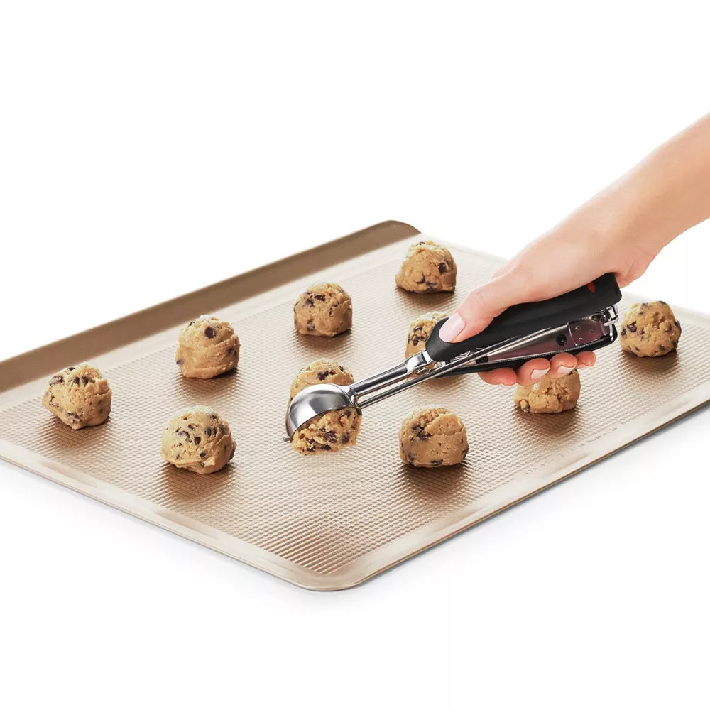 Hand using a cookie scoop to place chocolate chip cookie dough on a baking sheet.
