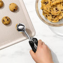 Cookie dough being scooped onto a baking sheet with a cookie scoop.
