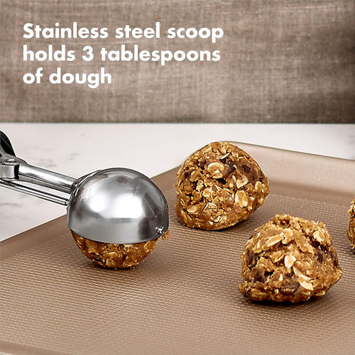 Cookie scoop placing cookie dough on a baking sheet with text 'stainless steel scoop holds 3 tablespoons of dough'