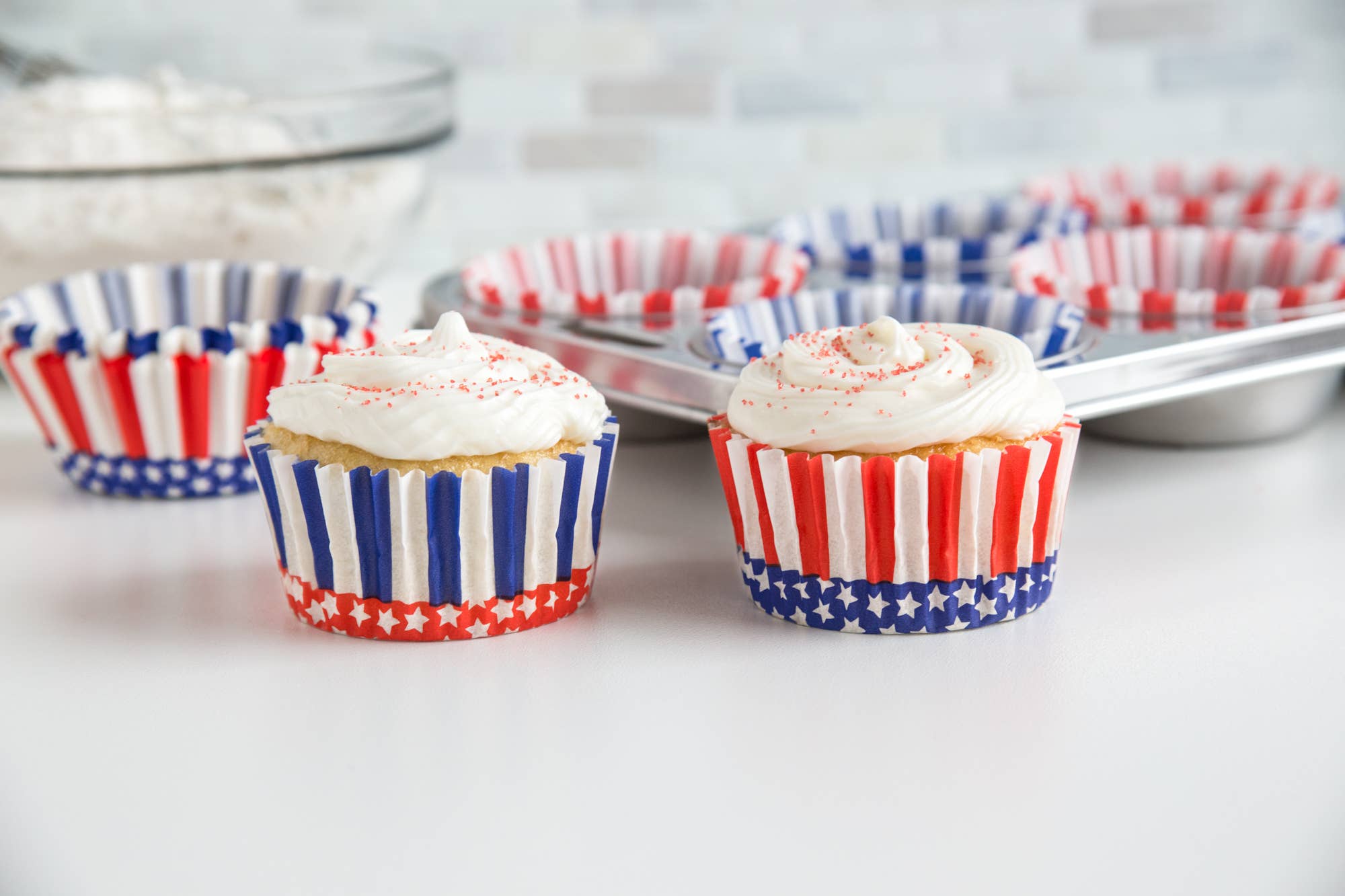 Cupcakes with white frosting in red, white, and blue striped cupcake liners on a light surface.