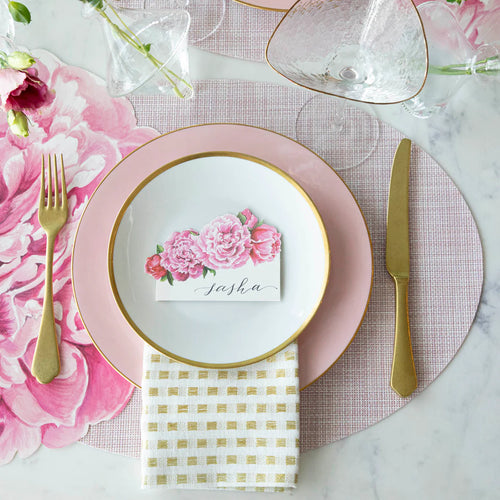 A place setting with a peony name card on a plate with pink and peony styled decor.