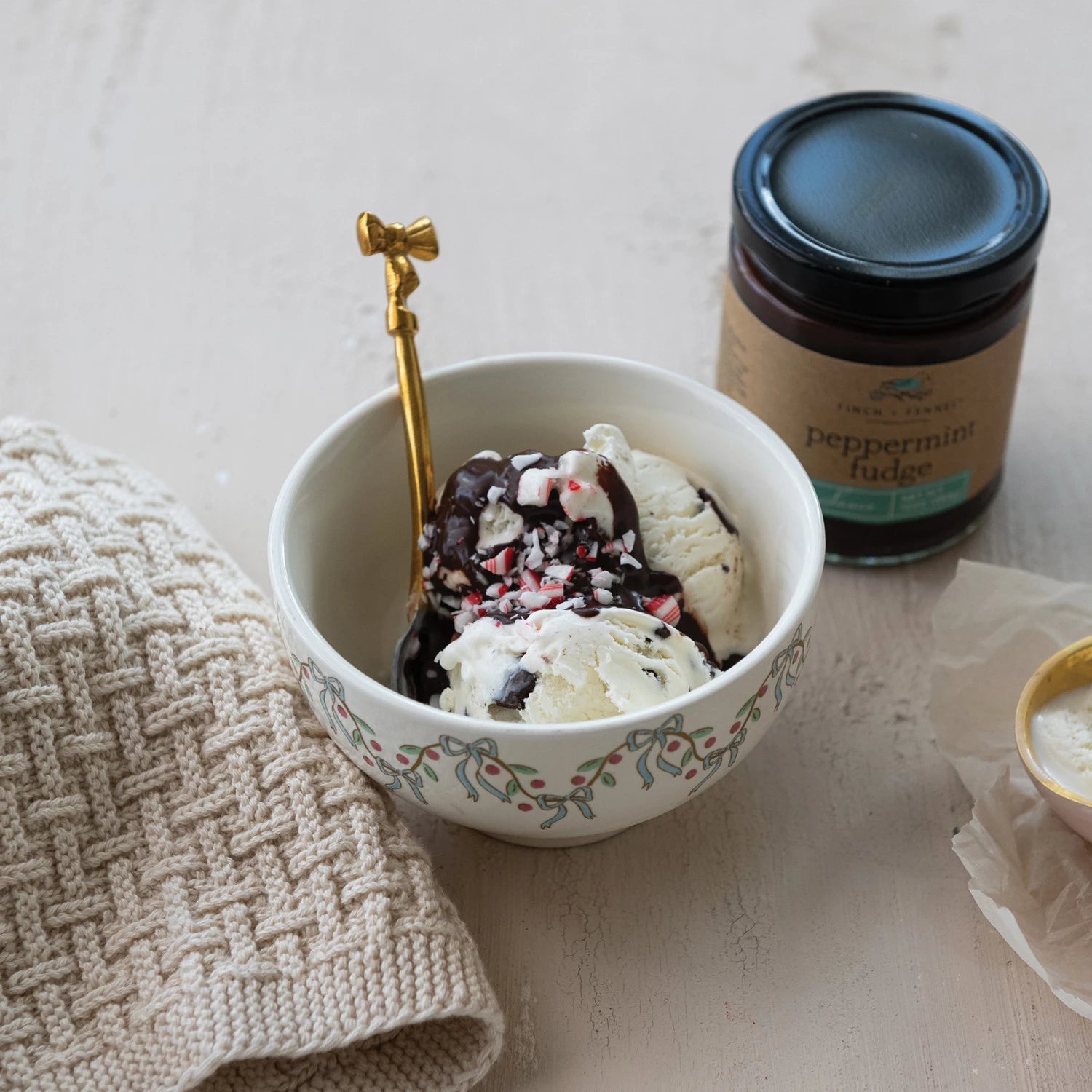 Bowl of ice cream with peppermint fudge on a light surface next to a jar of peppermint fudge.