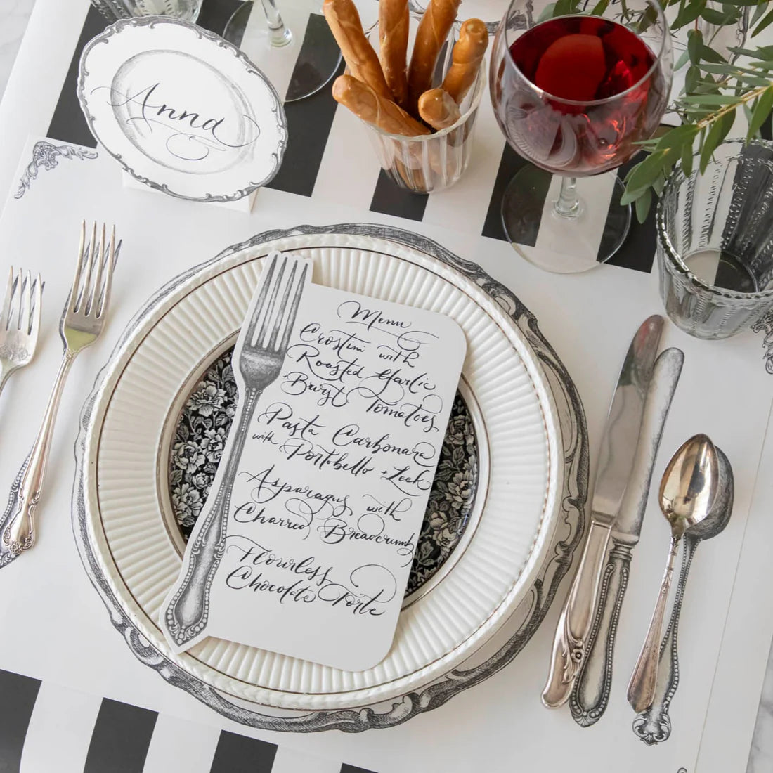 A place setting with silverware, plate, and black and white striped table runner.