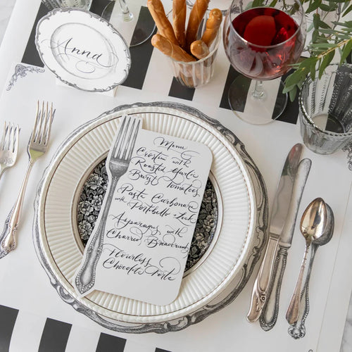A place setting with silverware, plate, and black and white striped table runner.