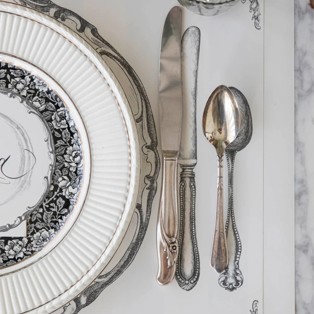 A close up of a plate, knife, and spoon on a paper placemat that features illustrations of a place setting.