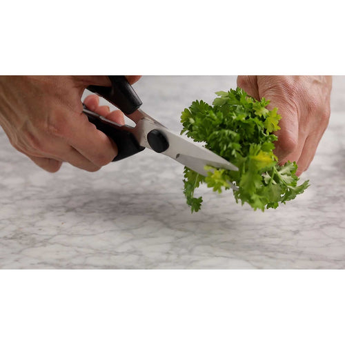 Person using kitchen shears to cut fresh greens on a marble surface