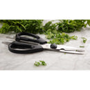 Black-handled scissors on a marble surface with fresh green herbs.