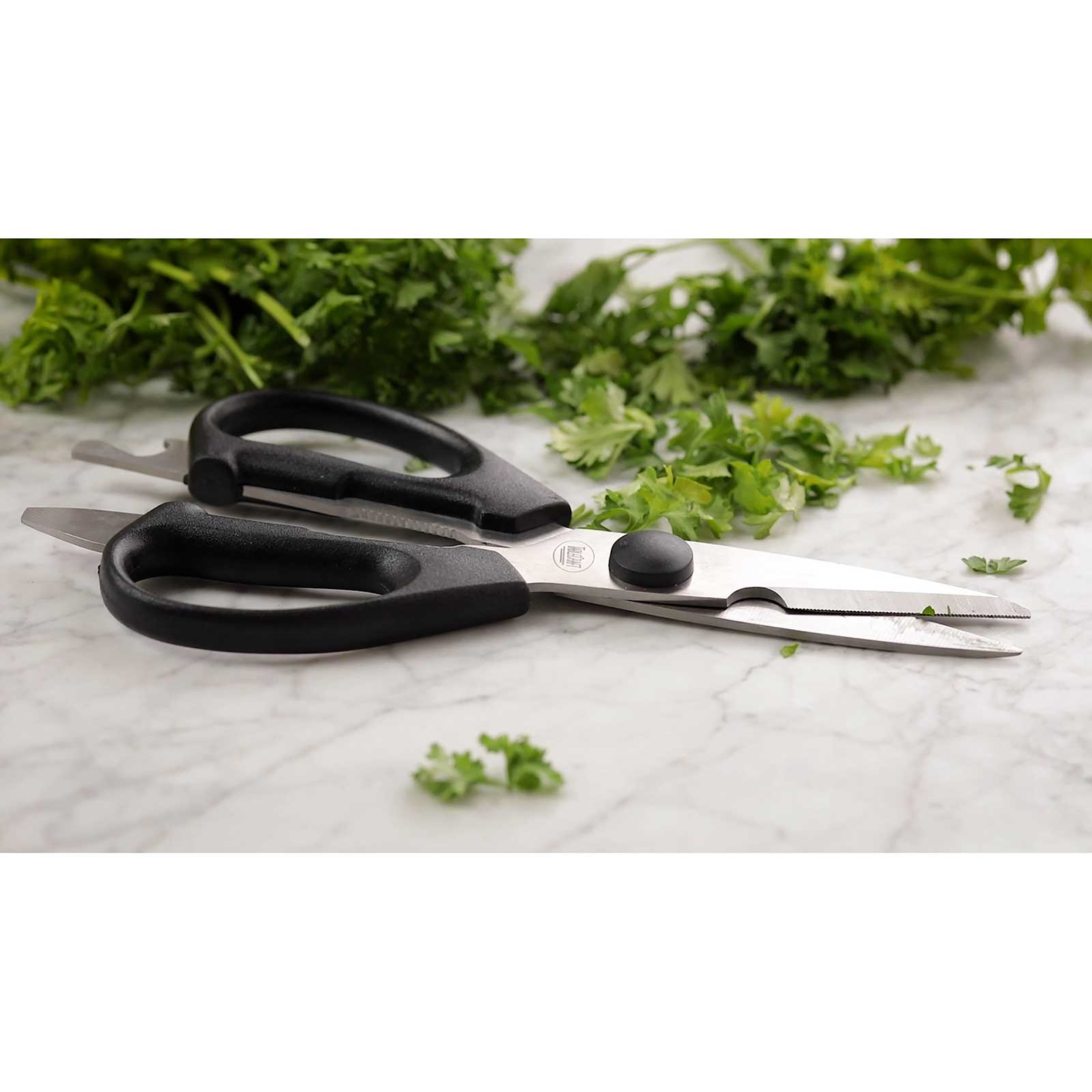 Black-handled scissors on a marble surface with fresh green herbs.