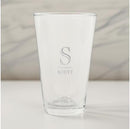 A clear glass pint glass with customizable text on it, placed on a marble surface.