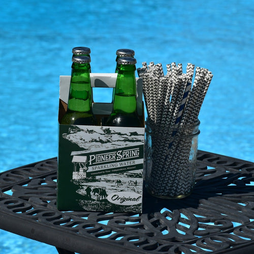 A case of Pioneer Spring Sparkling Water glass bottles placed on a table with a field in the background.