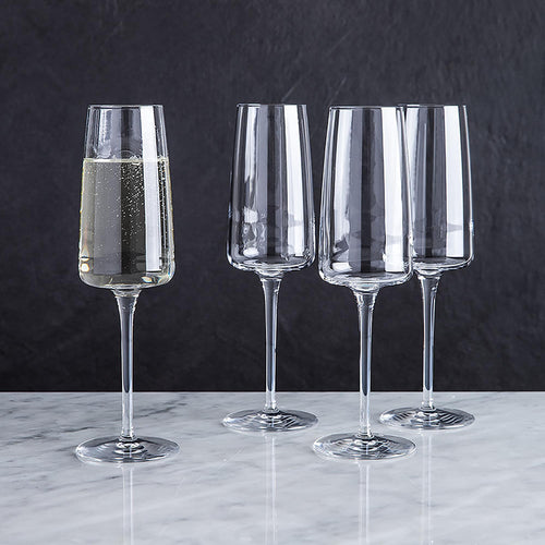 A set of four clear champagne flute glasses filled with liquid, displayed on a marble surface.