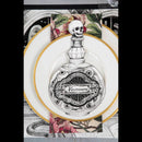 A decorative dinner plate featuring a black and white illustration of an ornate perfume bottle with a skull on the stopper and the word 'Nevermore' on the label. The plate is layered on top of a gold-rimmed plate and set against a patterned placemat with gothic illustrations.