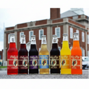 Multiple bottles of Polly's Pop soda in different flavors, displayed in front of a historical courthouse.
