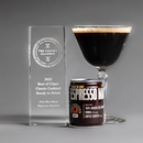 A glass award crystal plaque, a can of Espresso Martini liqueur, and a prepared espresso martini in a coupe glass, arranged on a gray studio background.