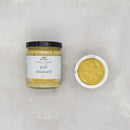 Jar of pub mustard with a small bowl of mustard on a light gray background