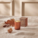 Copper-colored candle with decorative box and autumn leaves on a textured surface