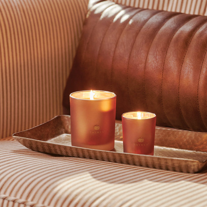 Two lit candles on a tray with a brown leather couch in the background