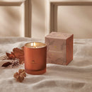 Candle with a lit wick and packaging on a textured surface