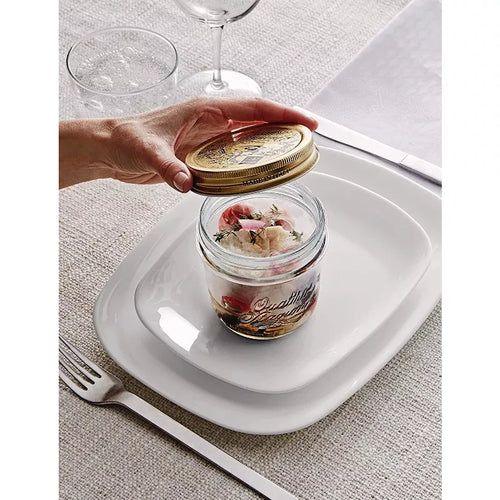 A mason jar with food inside on top of plates with a person holding the lid over it.