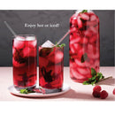 Two glasses and a pitcher filled with ice, mint leaves, and raspberry tea on a white surface with a gray background.
