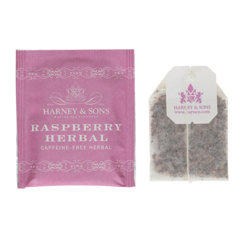 Packaging and a single tea bag from Harney & Sons Raspberry Herbal tea, displaying the blend of rosehips, hibiscus, orange peel, and raspberry.
