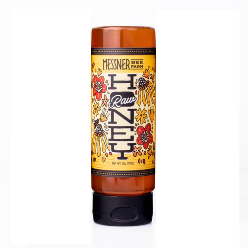 A squeeze bottle of Messner Bee Farm Raw Honey, featuring an amber-colored plastic bottle with a black cap and a yellow label decorated with floral illustrations.