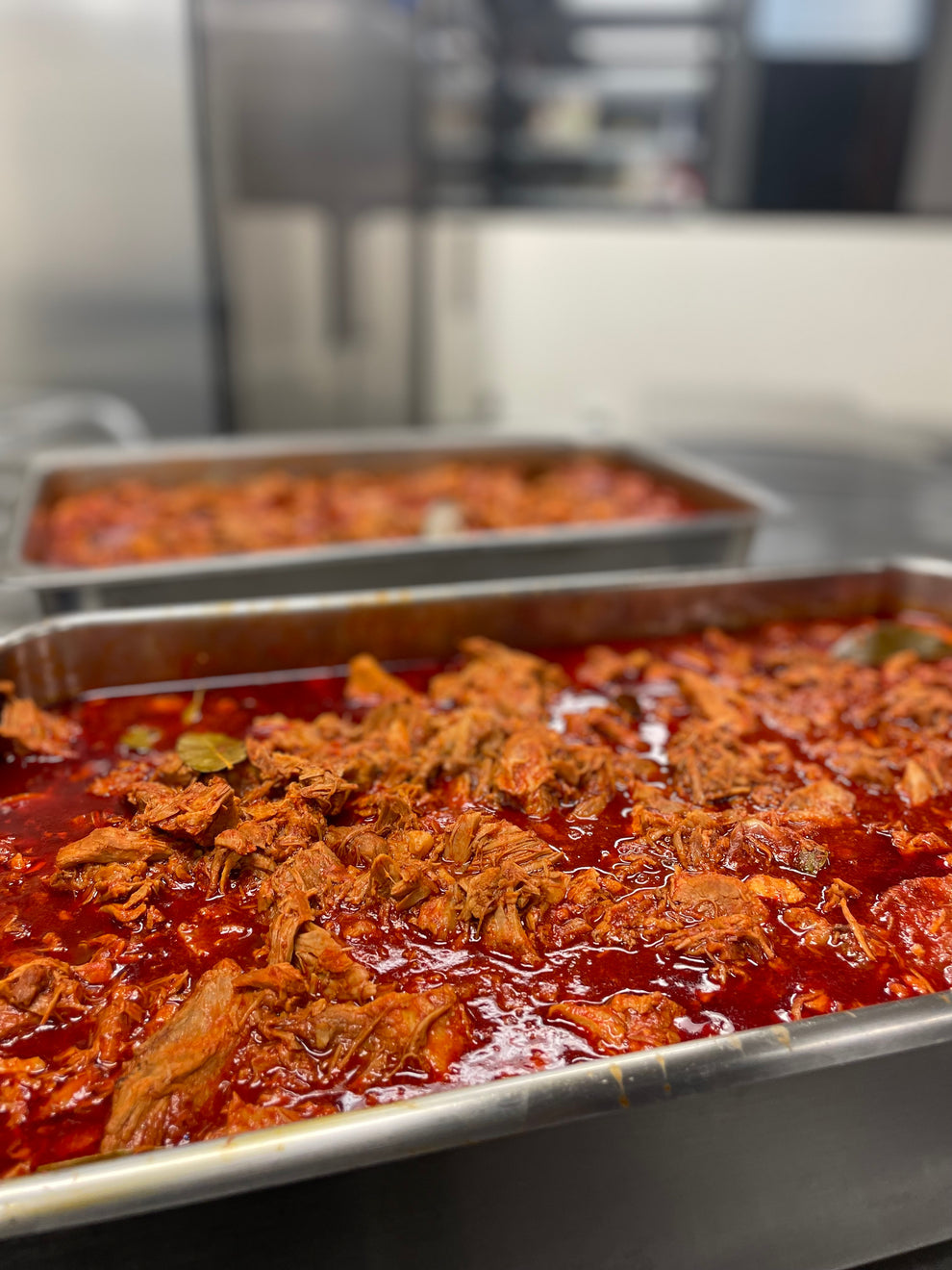 Metal trays with red sauce and meat in a kitchen setting