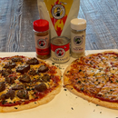Two pizzas on a neutral surface with pizza seasonings and sauce next to them all on a wooden table.
