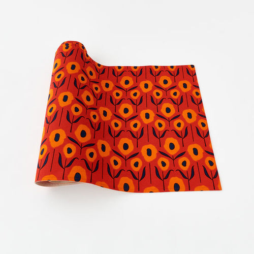 A red table runner with a geometric pattern of orange and navy poppies displayed on a white background.
