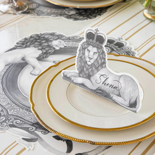 A place setting featuring regal lion placemat and lion wearing a crown place card on a gold and white striped table runner.