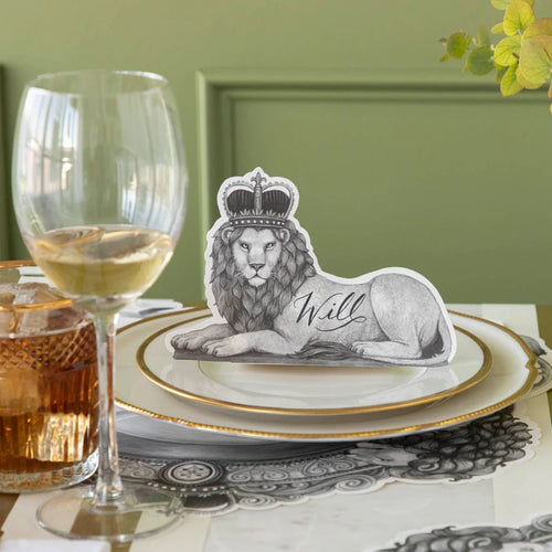 A regal lion wearing a crown place card on a pair of plates with a glass of wine.