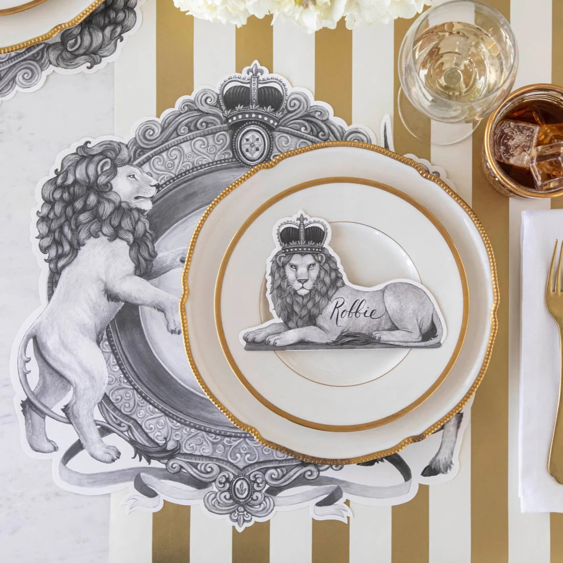 A place setting featuring regal lion placemat and lion wearing a crown place card on a gold and white striped table runner.
