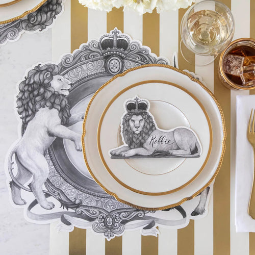 A place setting featuring regal lion placemat and lion wearing a crown place card on a gold and white striped table runner.